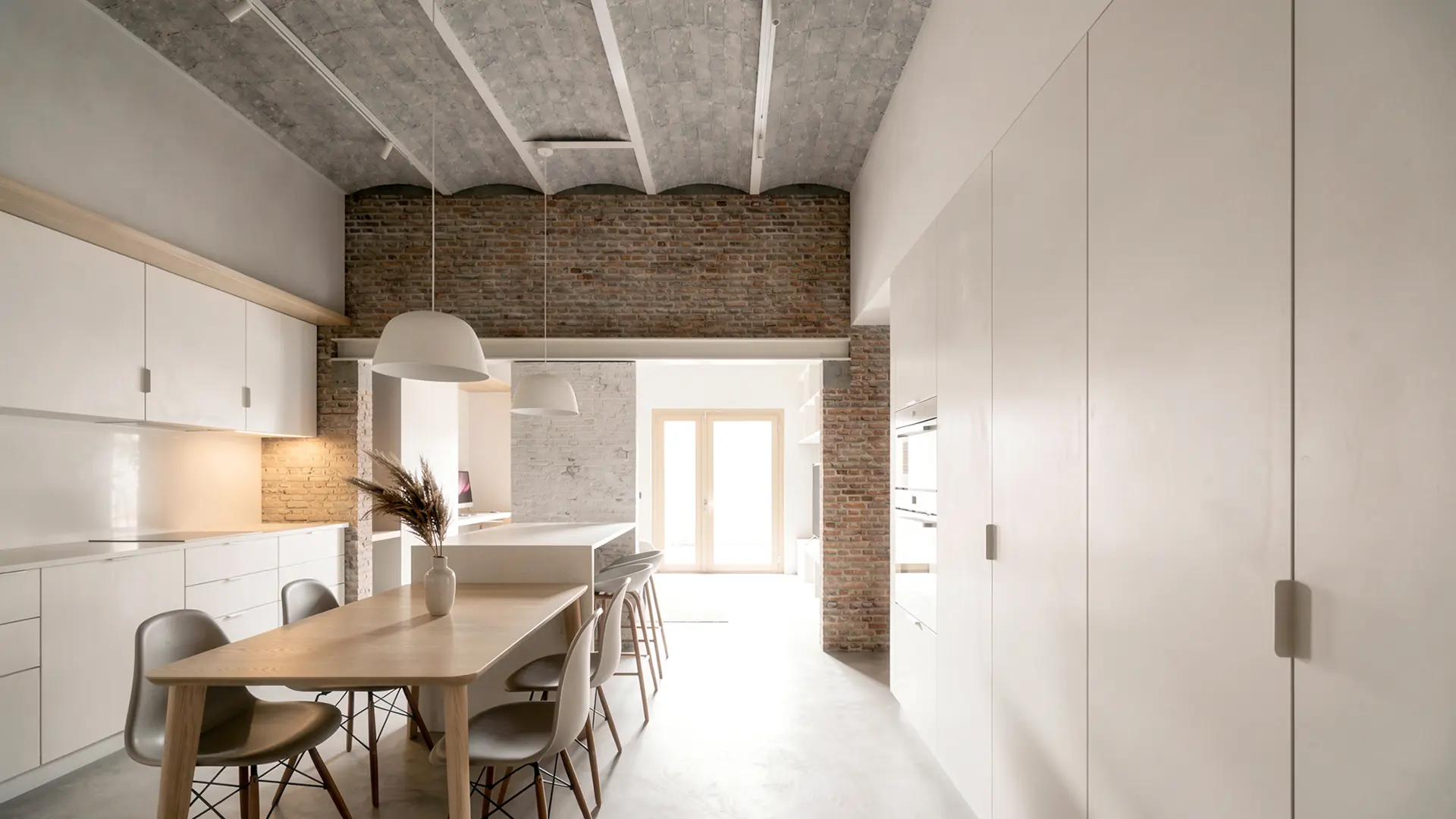 Cocina comedor de vivienda reformada en Badalona, con muebles lacados en blanco, techo de bóveda catalana con vigas de hormigón visto y paredes de ladrillo antiguo recuperado. Proyecto de Tova Arquitectura
