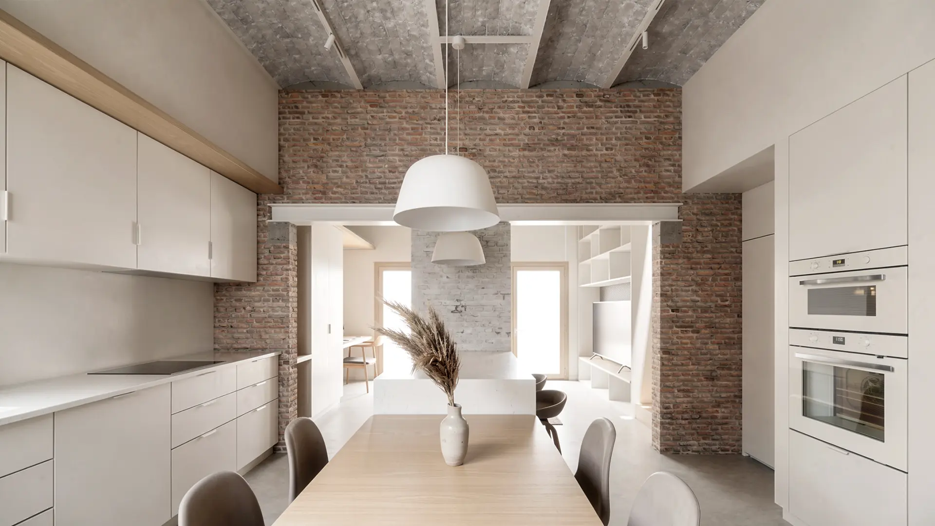Cocina comedor de vivienda reformada en Badalona, con muebles lacados en blanco, techo de bóveda catalana con vigas de hormigón visto y paredes de ladrillo antiguo recuperado. Proyecto de Tova Arquitectura