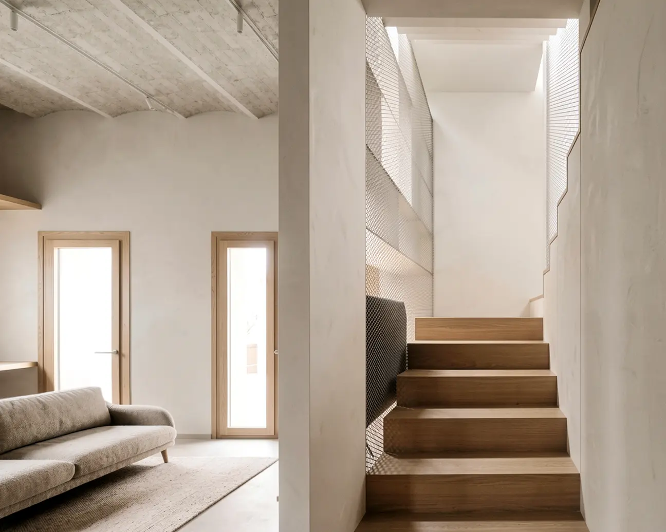 Escalera interior de vivienda reformada en Badalona, con peldaños de madera maciza, barandilla de malla metálica y lucernario cenital, junto a salón con techo de bóveda catalana y carpinterías de madera. Proyecto de Tova Arquitectura