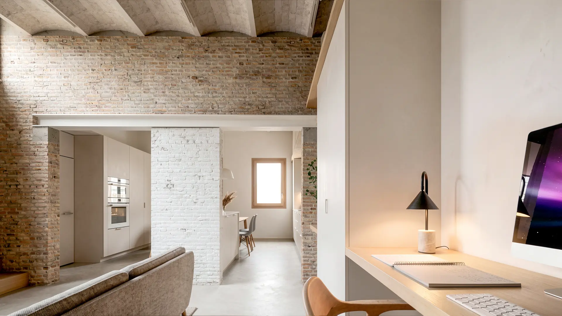 Zona de estudio integrada en vivienda reformada en Badalona, con escritorio de madera empotrado, techo de bóveda catalana y ladrillo antiguo recuperado visto en contraste con acabados blancos y suelo de microcemento. Proyecto de Tova Arquitectura.
