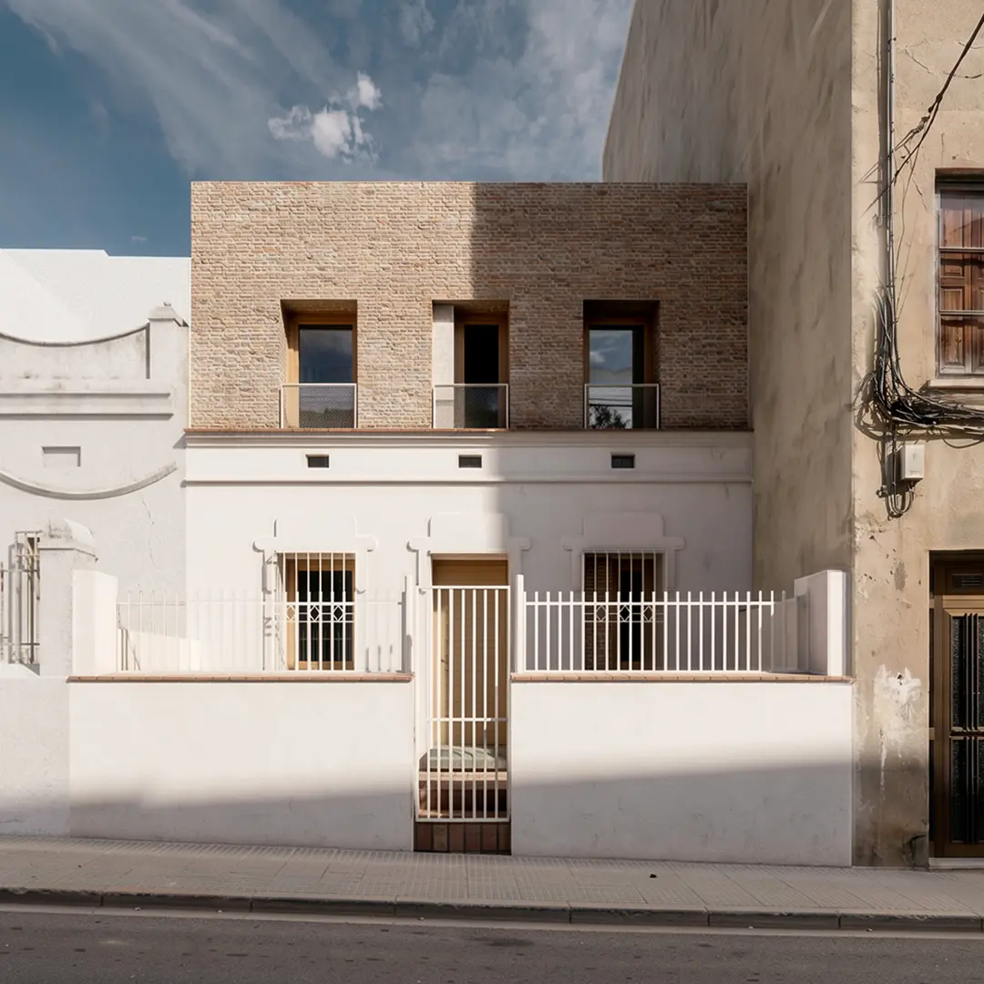 Fachada de vivienda reformada en Badalona, con ampliación de planta superior en ladrillo visto cara vista y carpinterías de madera, integrada en tejido urbano histórico. Proyecto de Tova Arquitectura
