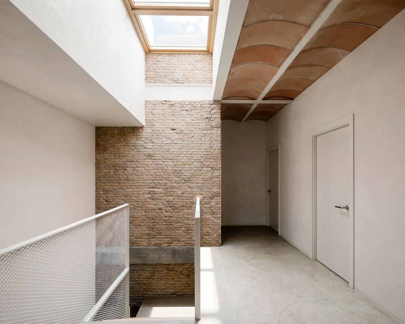 Núcleo de escalera de vivienda reformada en Badalona, con lucernario cenital, techo de bóveda catalana de rasilla vista, barandilla de malla metálica y carpinterías de madera. Proyecto de Tova Arquitectura