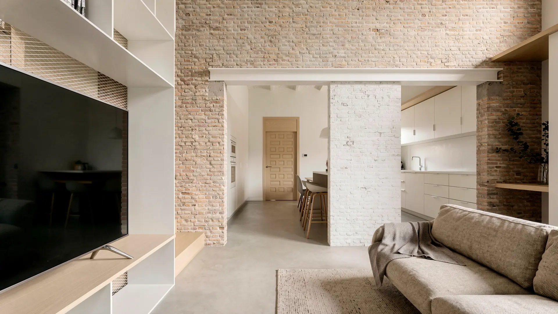 Planta abierta de salón y cocina en vivienda reformada en Badalona, con ladrillo antiguo recuperado visto en contraste con acabados blancos, suelo de microcemento y carpintería de madera original restaurada. Proyecto de Tova Arquitectura