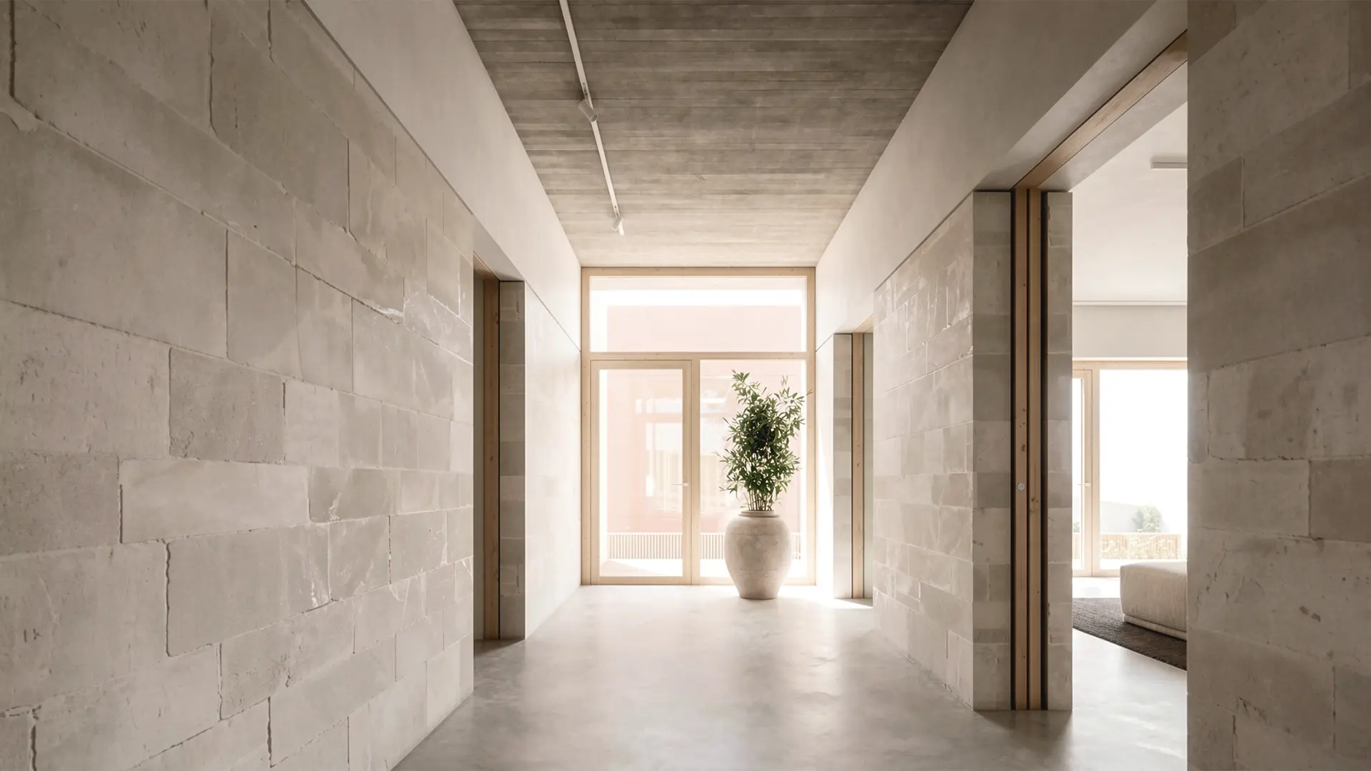 Entrada interior de vivienda unifamiliar de obra nueva en L'Ametlla del Vallès, con paredes y techo de piedra natural vista, suelo de microcemento y carpinterías de madera que enmarcan la salida al jardín. Proyecto de Tova Arquitectura
