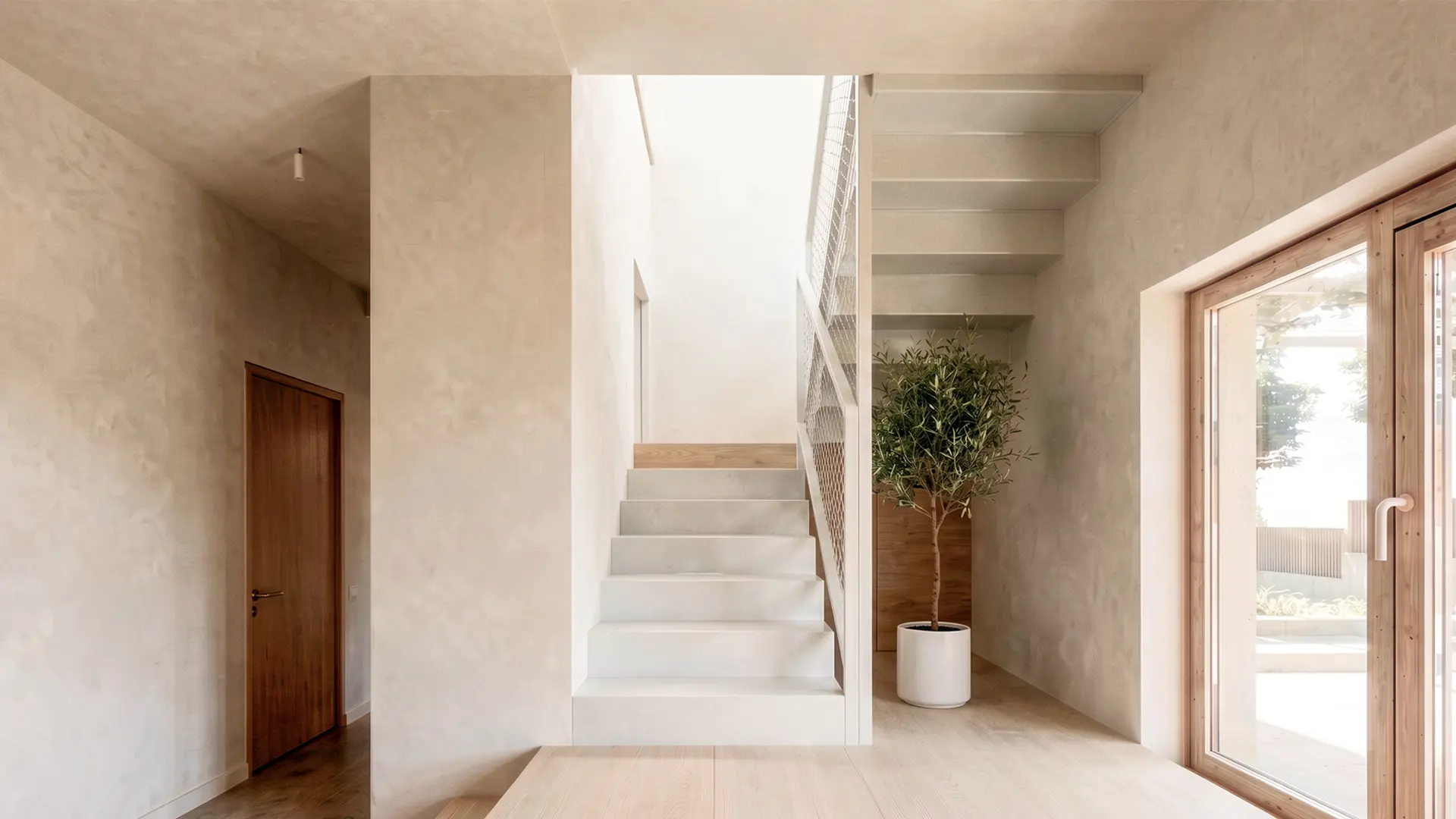 Escalera interior de vivienda unifamiliar de obra nueva en L'Ametlla del Vallès, con peldaños de microcemento, barandilla de malla metálica y lucernario cenital que inunda el núcleo de luz natural. Proyecto de Tova Arquitectura