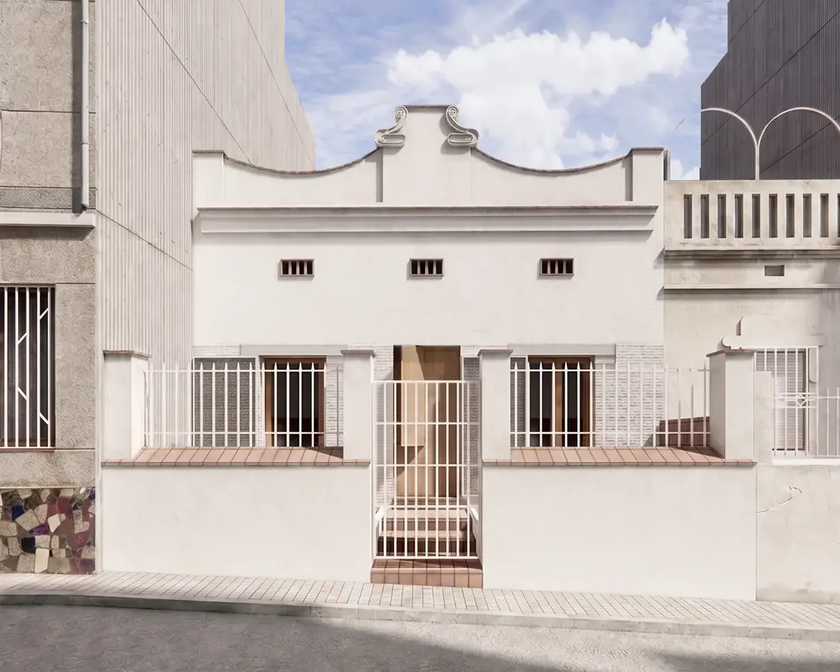 Fachada principal de vivienda reformada en Badalona, con remate modernista original restaurado, acabado encalado en blanco, carpinterías de madera y verja metálica de acceso. Proyecto de Tova Arquitectura