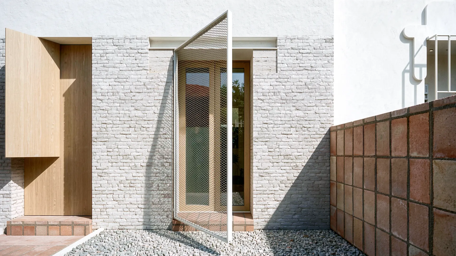 Detalle de fachada de vivienda reformada en Badalona, con ladrillo antiguo recuperado visto, contraventana de malla metálica abatible, carpintería de madera y cerramiento de gres cerámico. Proyecto de Tova Arquitectura