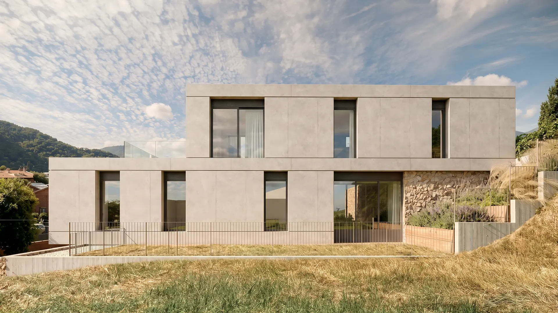 Fachada posterior de vivienda unifamiliar de obra nueva en Cardedeu, con volumen de dos plantas en hormigón visto, zócalo de mampostería de piedra natural y vistas al Montseny. Propuesta de diseño de Tova Arquitectura
